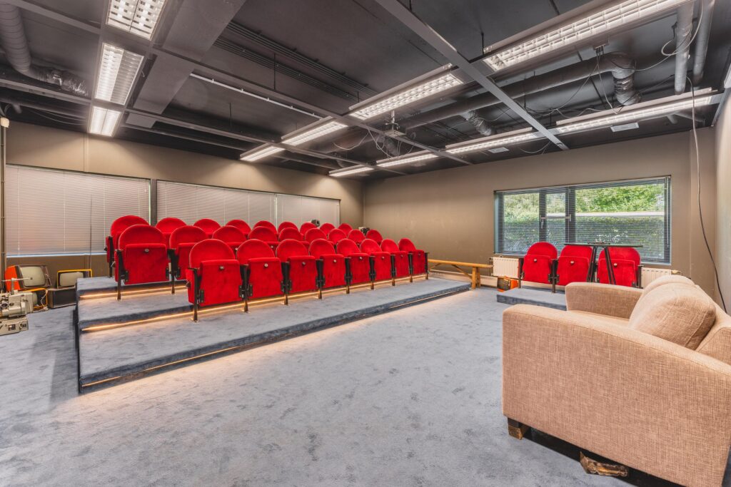 Kleine presentatieruimte met rode theaterstoelen en een beige bank in een modern interieur aan de Prof. W.H. Keesomlaan.